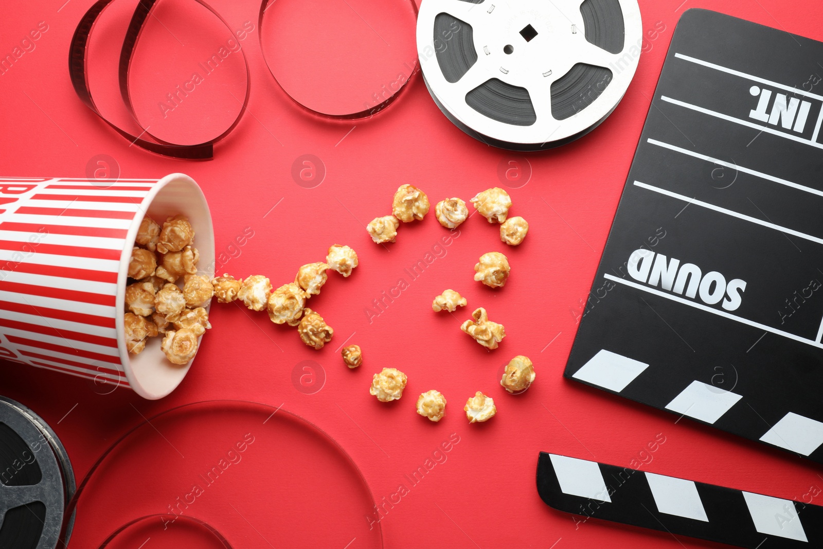 Photo of Movie clapper, sweet popcorn and film reels on red background, flat lay