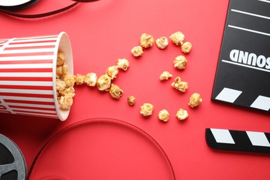 Movie clapper, sweet popcorn and film reels on red background, flat lay