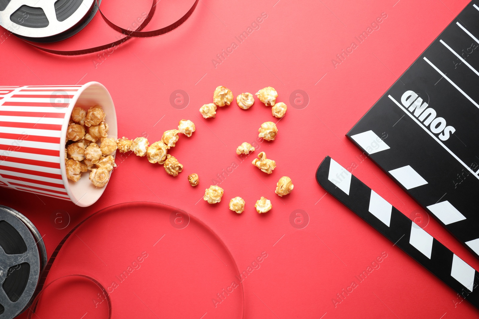 Photo of Movie clapper, sweet popcorn and film reels on red background, flat lay