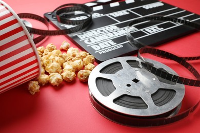 Photo of Movie clapper, sweet popcorn and film reel on red background, closeup