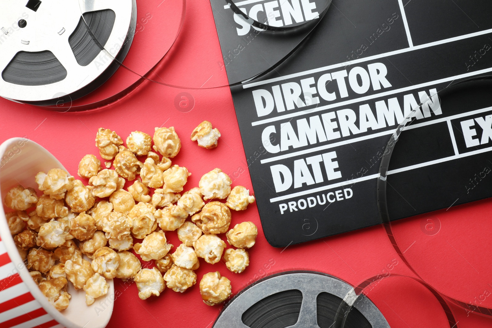 Photo of Movie clapper, sweet popcorn and film reels on red background, flat lay