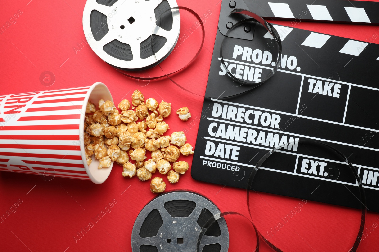 Photo of Movie clapper, sweet popcorn and film reels on red background, flat lay