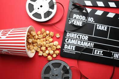 Photo of Movie clapper, sweet popcorn and film reels on red background, flat lay