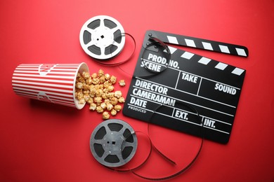 Movie clapper, sweet popcorn and film reels on red background, flat lay