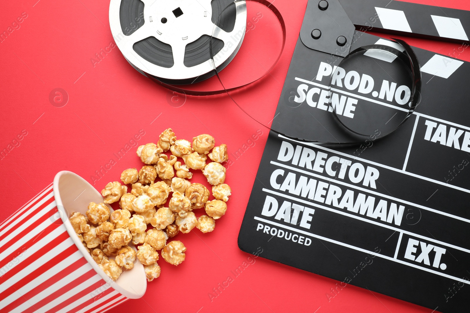 Photo of Movie clapper, sweet popcorn and film reel on red background, flat lay