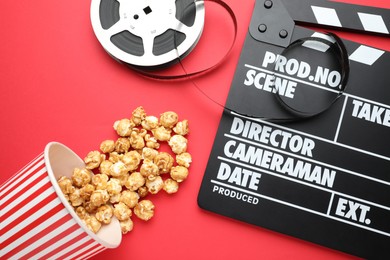 Photo of Movie clapper, sweet popcorn and film reel on red background, flat lay