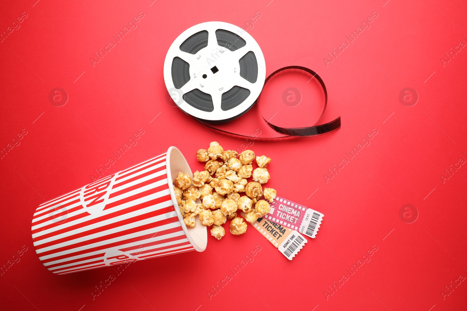 Photo of Sweet popcorn, movie tickets and film reel on red background, flat lay