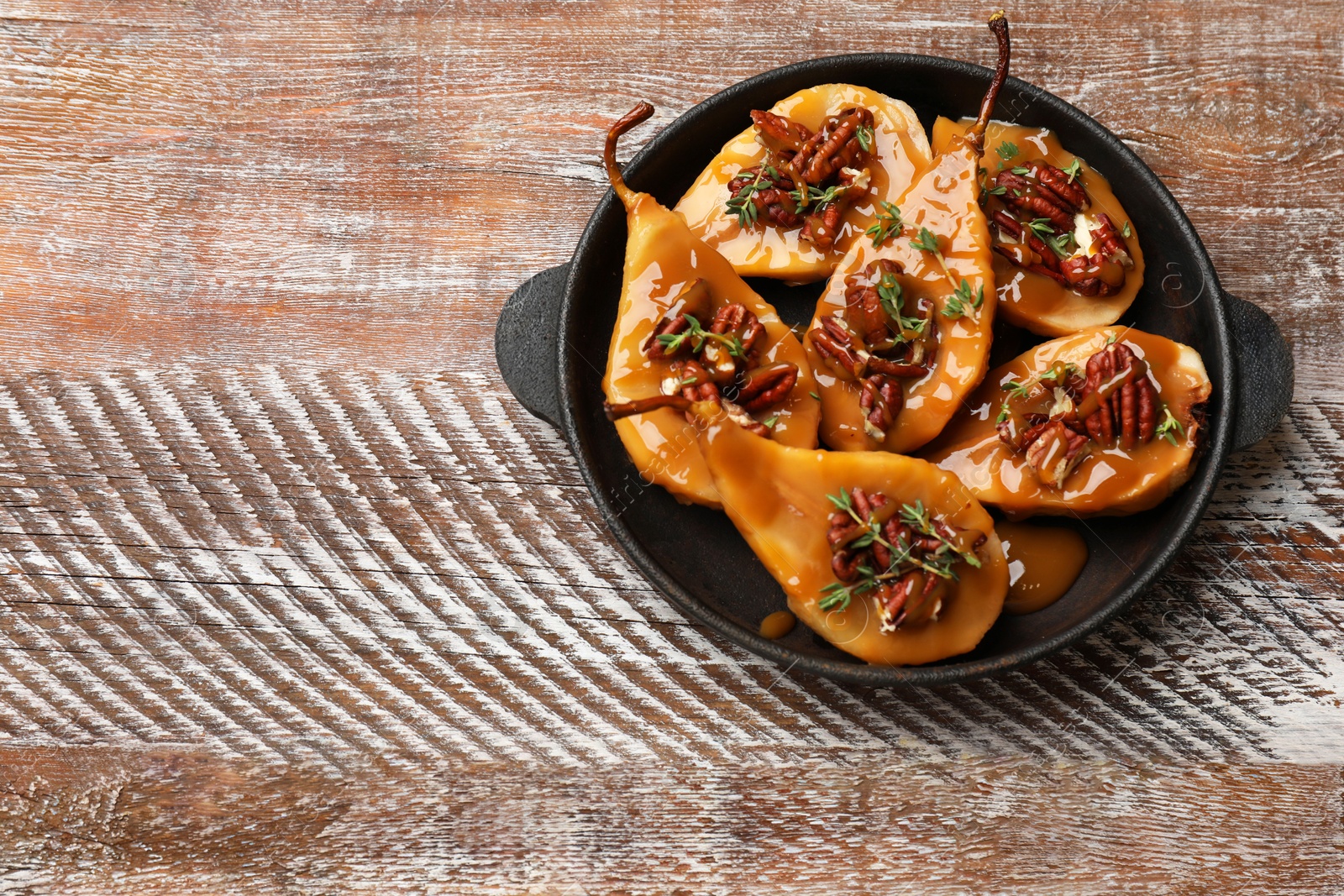 Photo of Delicious pears with caramel sauce, pecan nuts and thyme on wooden table, top view. Space for text