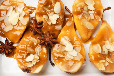 Photo of Delicious pears with caramel sauce, almond flakes and anise stars in baking dish, top view