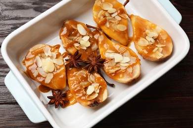 Photo of Delicious pears with caramel sauce, almond flakes and anise stars in baking dish on wooden table, top view