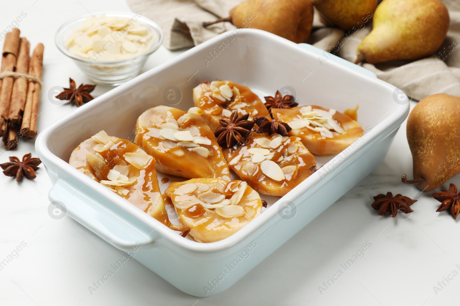 Photo of Delicious pears with caramel sauce, almond flakes and spices on white marble table, closeup