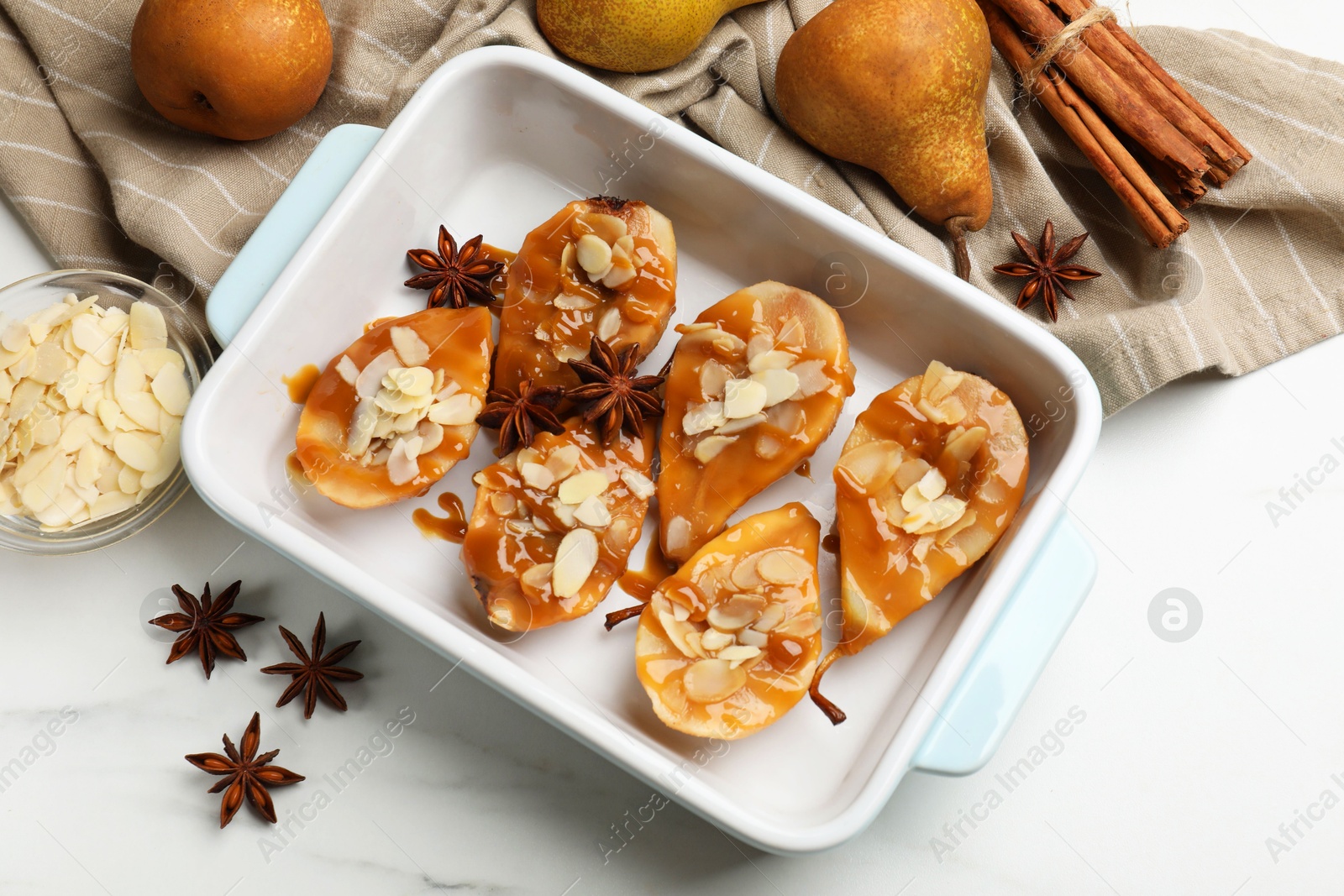 Photo of Delicious pears with caramel sauce, almond flakes and spices on white marble table, flat lay