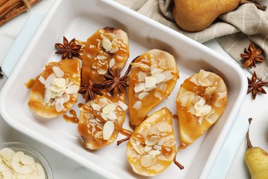 Photo of Delicious pears with caramel sauce, almond flakes and spices on white marble table, flat lay