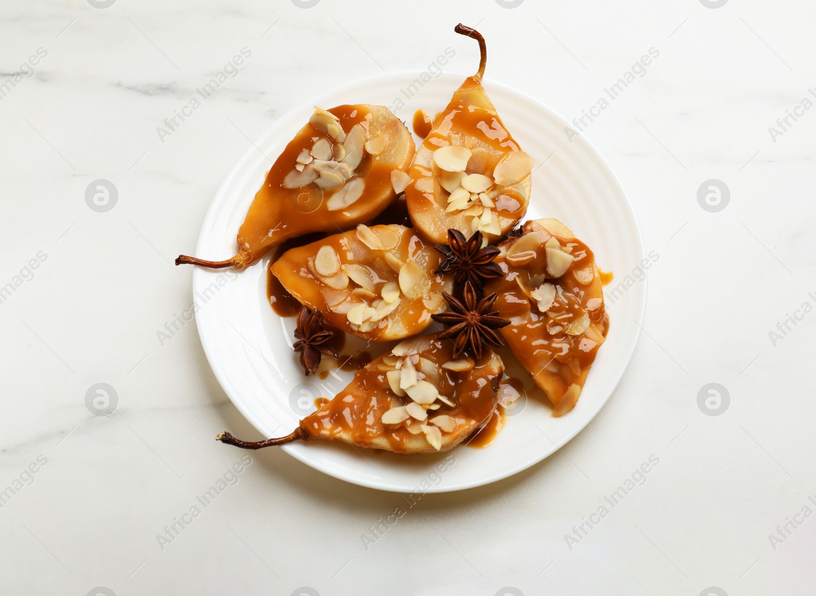 Photo of Delicious pears with caramel sauce, almond flakes and anise stars on white marble table, top view