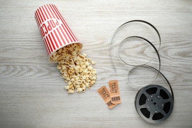 Photo of Tasty popcorn, tickets and film reel on white wooden background, flat lay