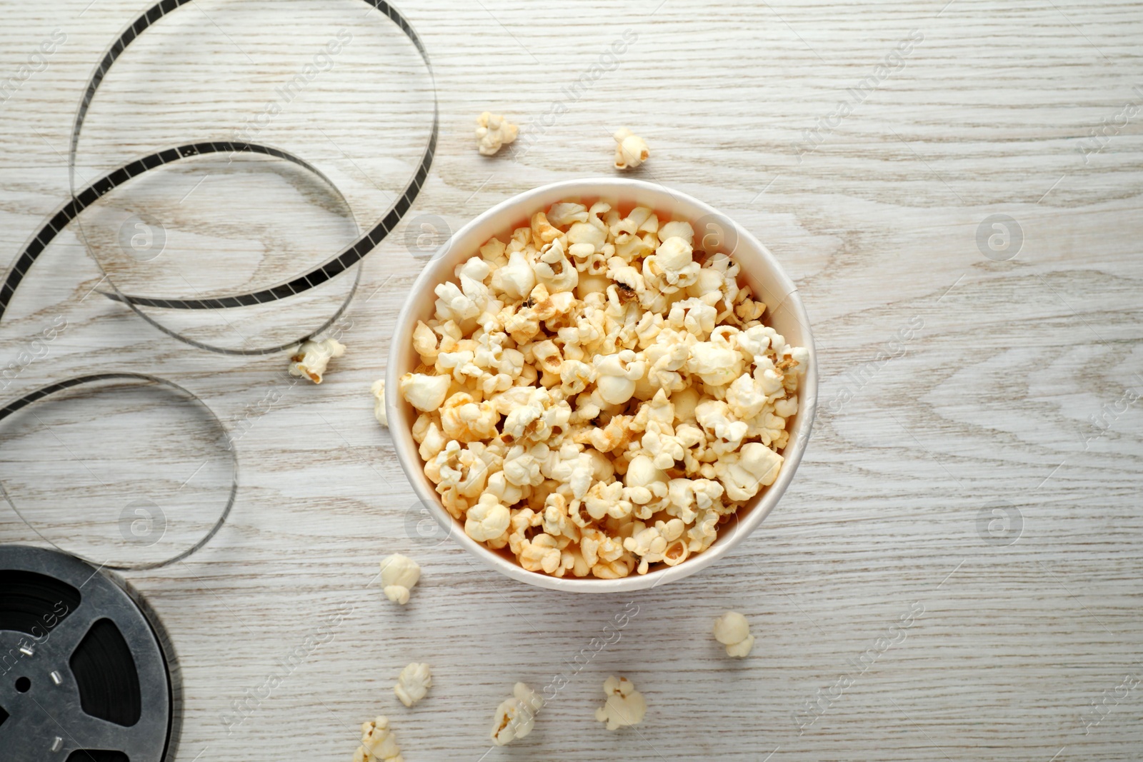 Photo of Tasty popcorn and film reel on white wooden background, flat lay