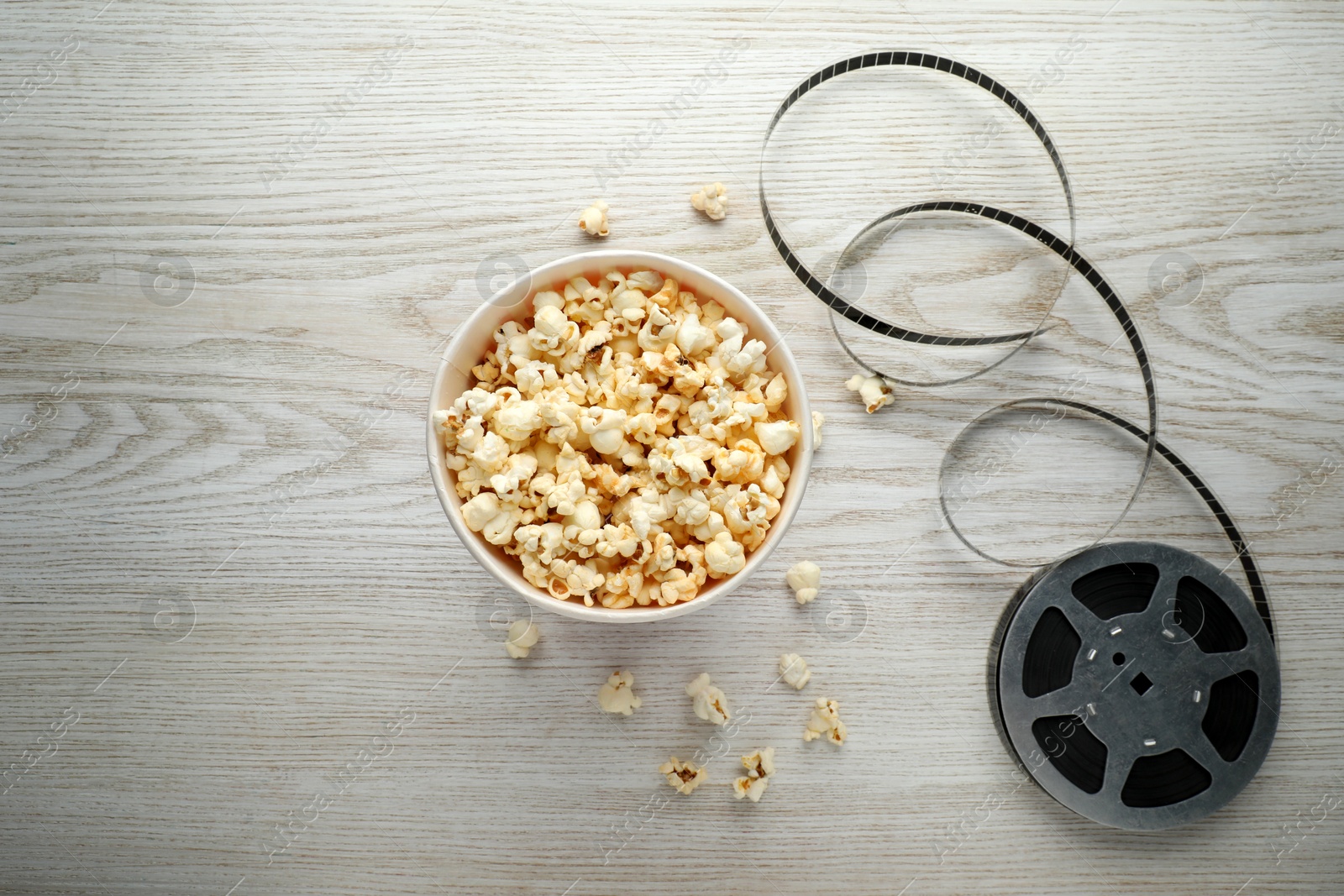 Photo of Tasty popcorn and film reel on white wooden background, flat lay