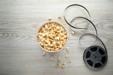 Photo of Tasty popcorn and film reel on white wooden background, flat lay