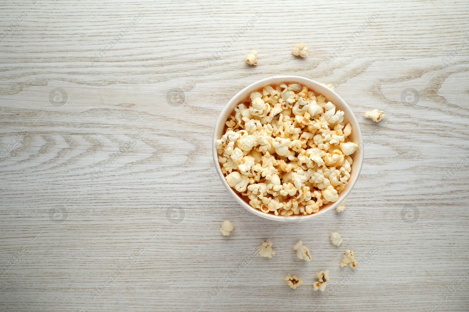 Photo of Tasty popcorn in paper cup on white wooden background, top view