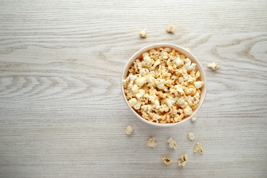 Photo of Tasty popcorn in paper cup on white wooden background, top view