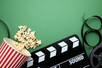 Photo of Movie clapper, tasty popcorn and film reel on green background, flat lay. Space for text