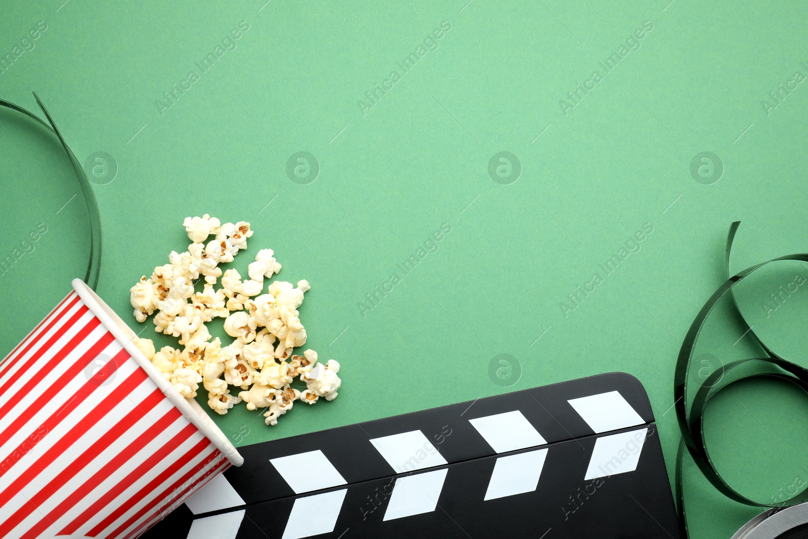 Photo of Movie clapper, tasty popcorn and film reel on green background, flat lay. Space for text