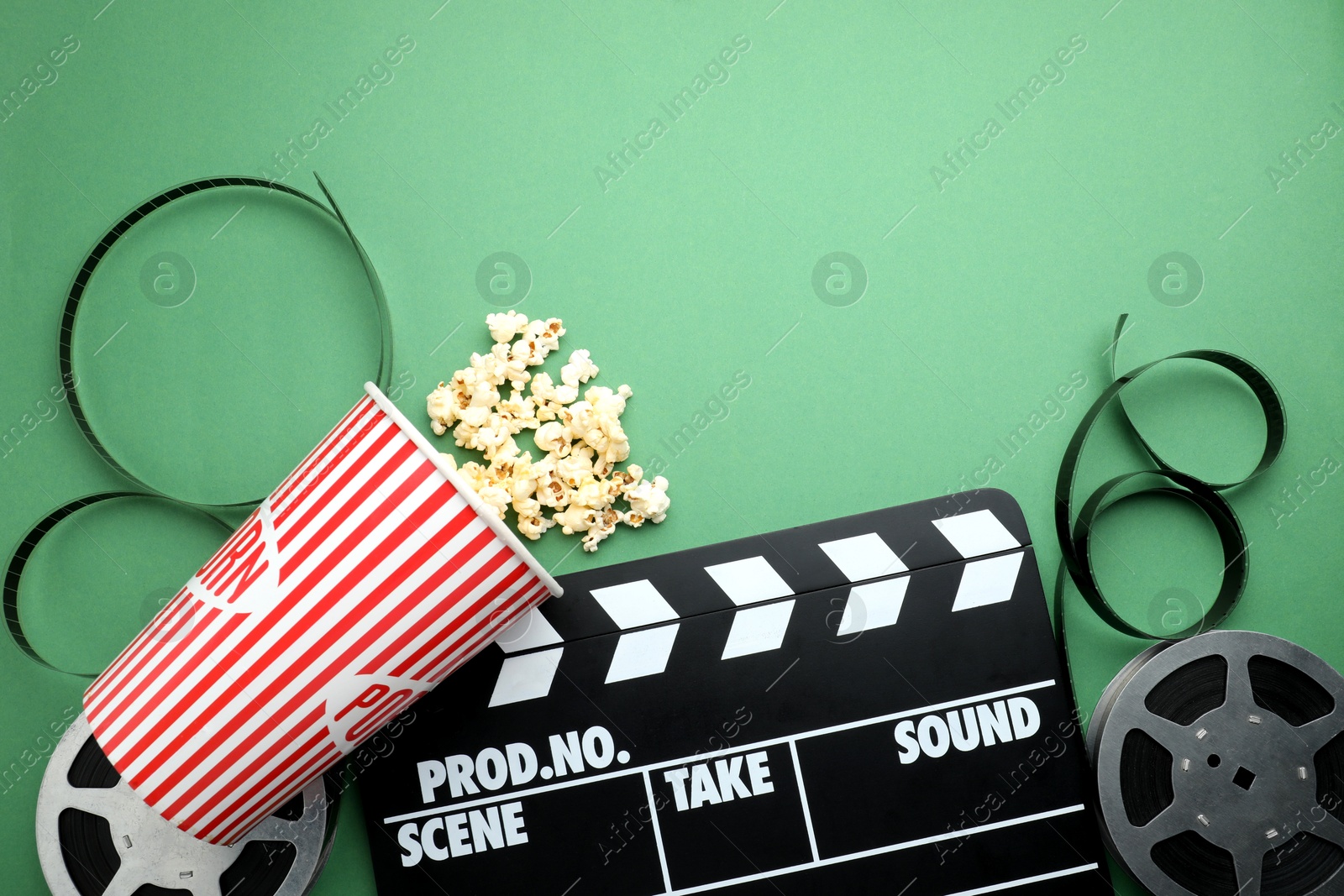 Photo of Movie clapper, tasty popcorn and film reel on green background, flat lay. Space for text