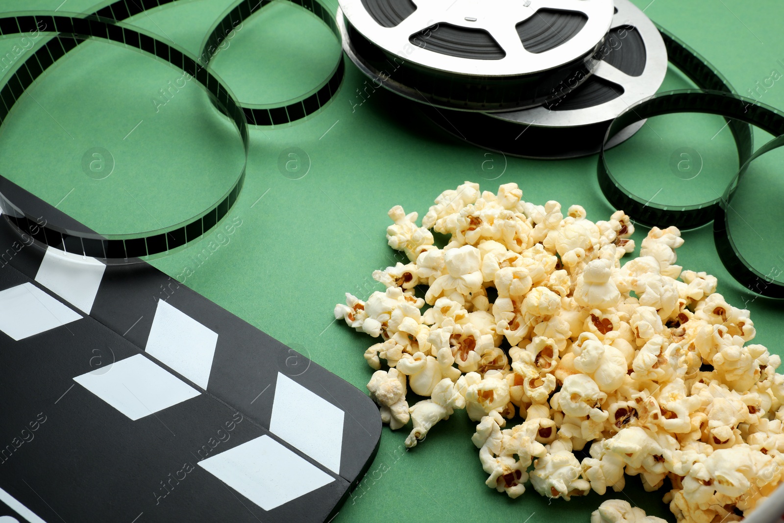 Photo of Movie clapper, tasty popcorn and film reel on green background, closeup