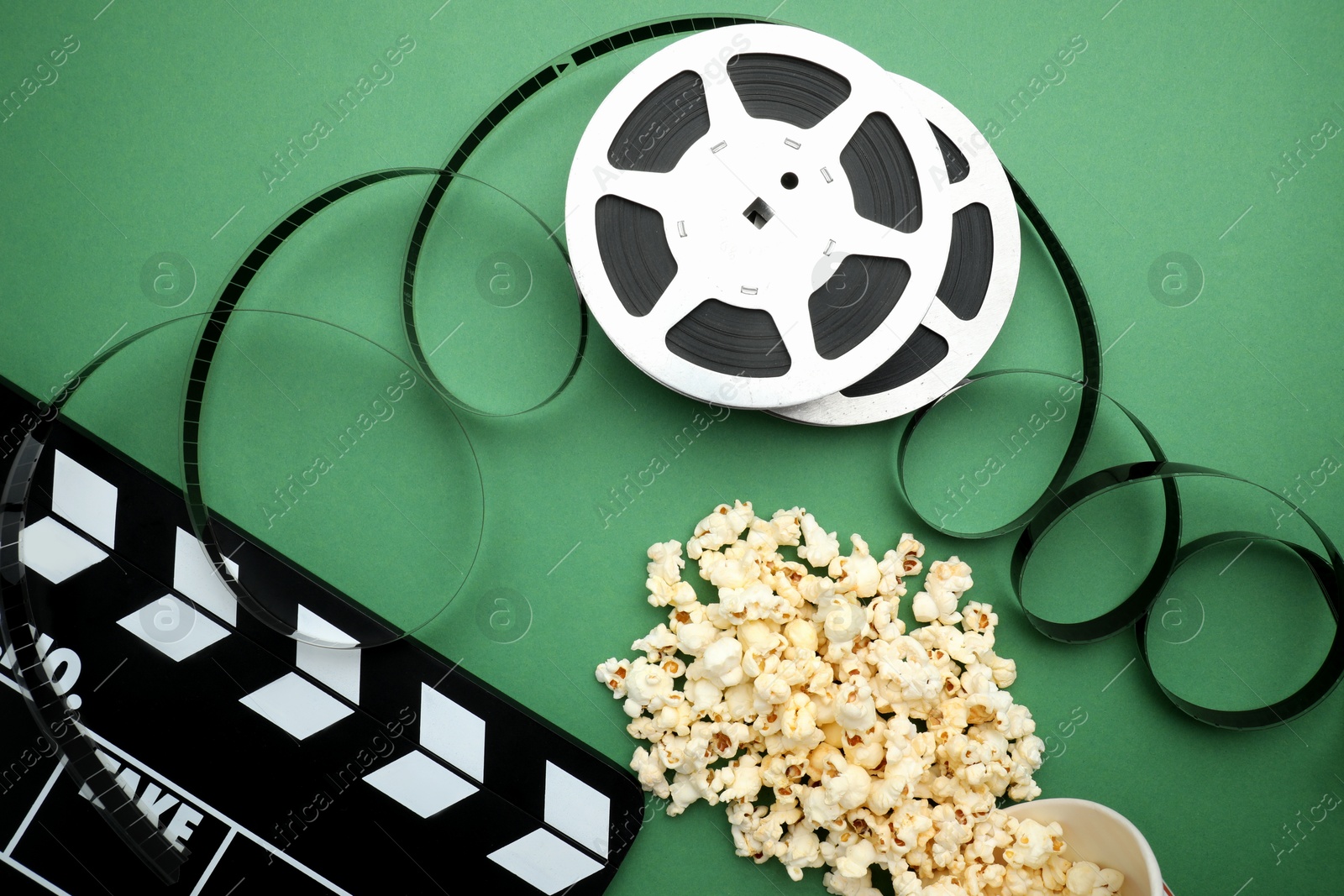 Photo of Movie clapper, tasty popcorn and film reel on green background, flat lay