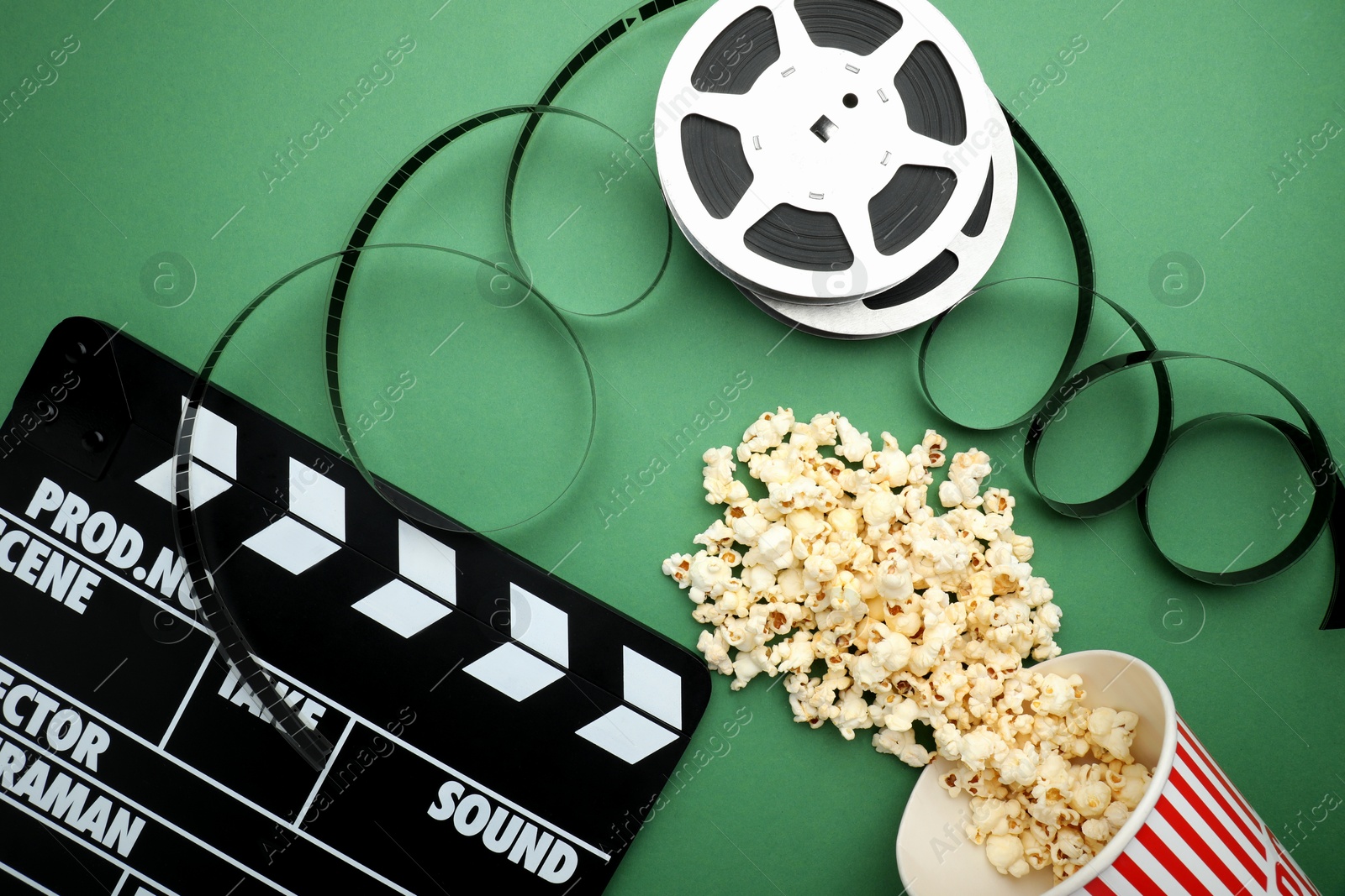 Photo of Movie clapper, tasty popcorn and film reel on green background, flat lay