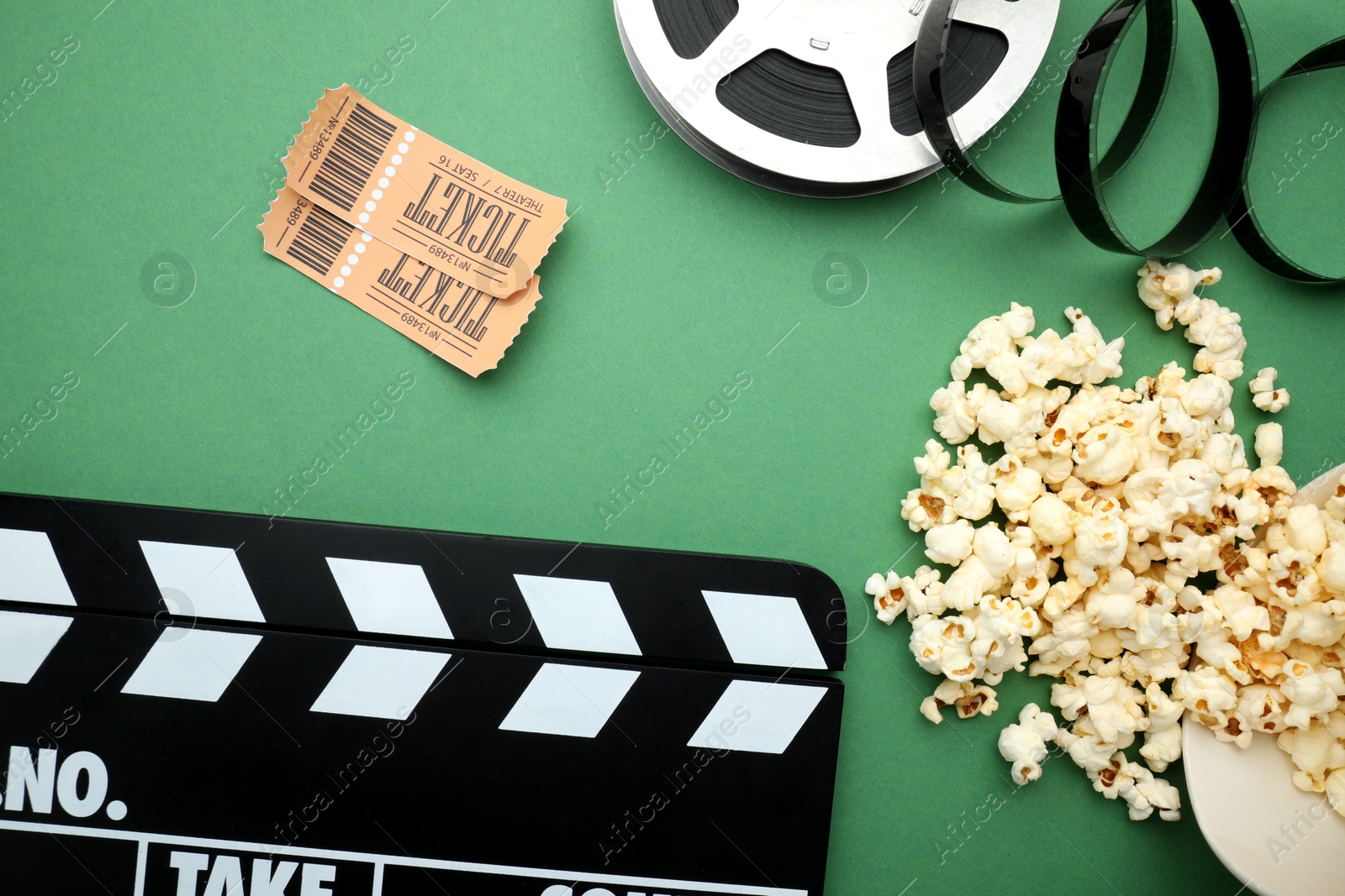 Photo of Movie clapper, tasty popcorn, tickets and film reel on green background, flat lay