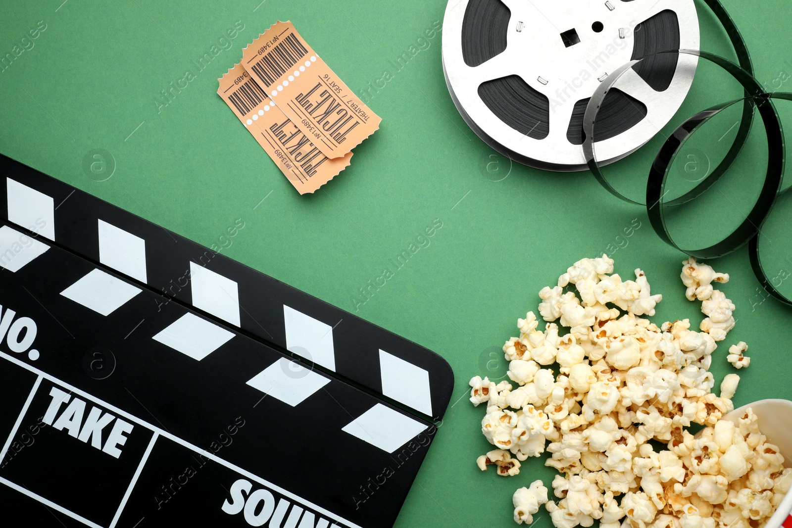 Photo of Movie clapper, tasty popcorn, tickets and film reel on green background, flat lay