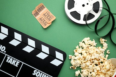 Photo of Movie clapper, tasty popcorn, tickets and film reel on green background, flat lay