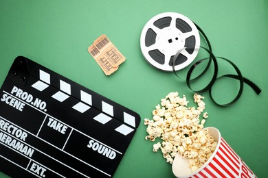 Photo of Movie clapper, tasty popcorn, tickets and film reel on green background, flat lay