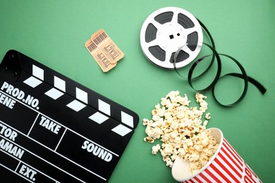 Photo of Movie clapper, tasty popcorn, tickets and film reel on green background, flat lay