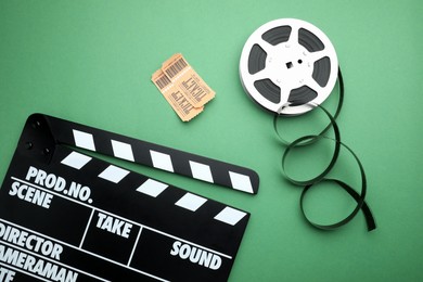 Photo of Movie clapper, tickets and film reel on green background, flat lay