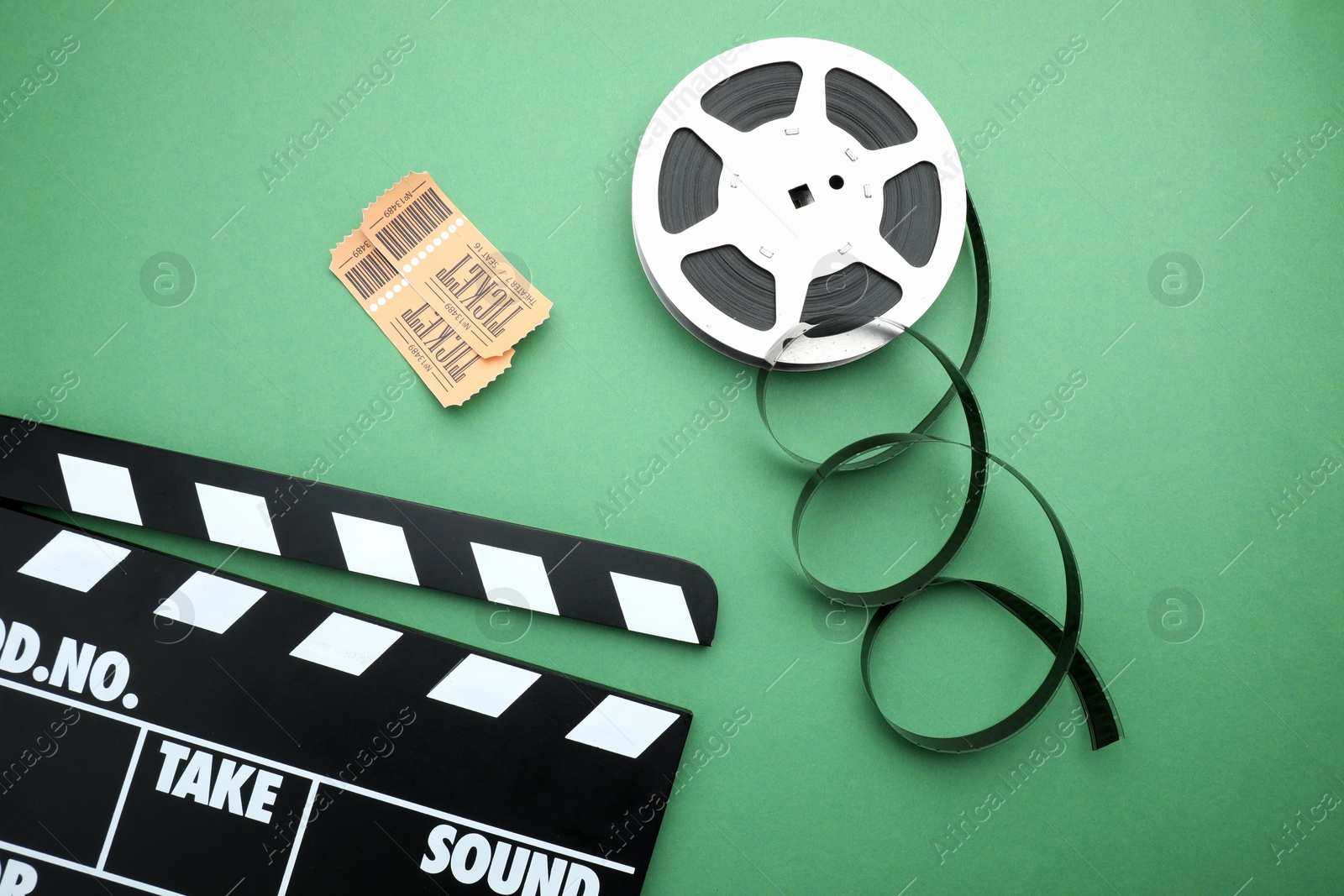 Photo of Movie clapper, tickets and film reel on green background, flat lay