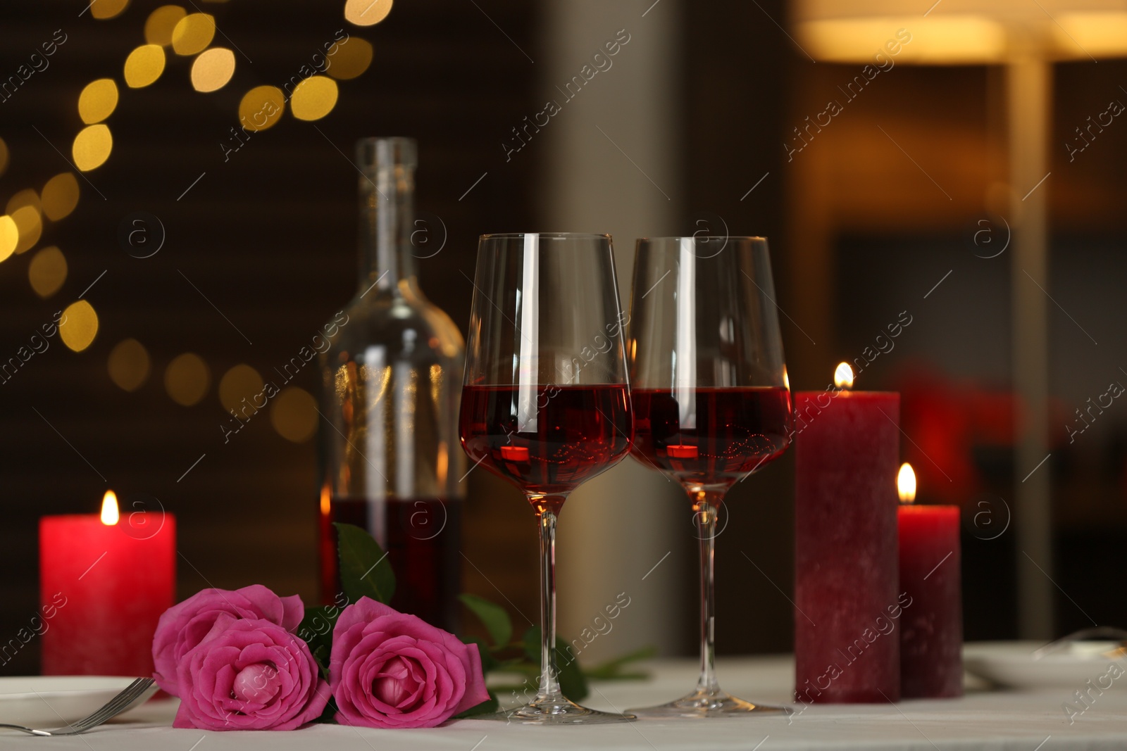 Photo of Romantic table setting with red wine, burning candles and roses in restaurant