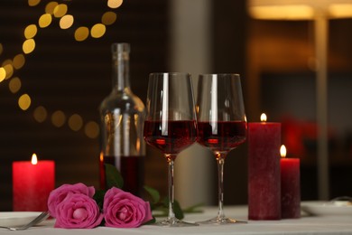 Photo of Romantic table setting with red wine, burning candles and roses in restaurant