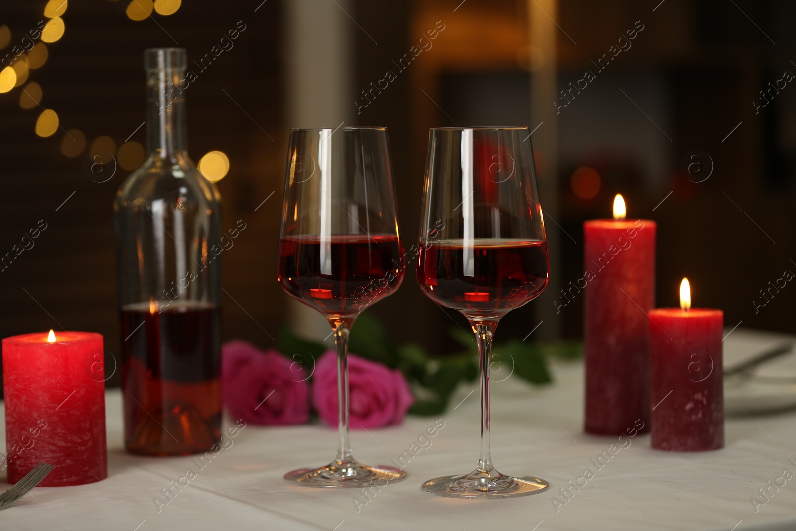 Photo of Romantic place setting with red wine and burning candles on table