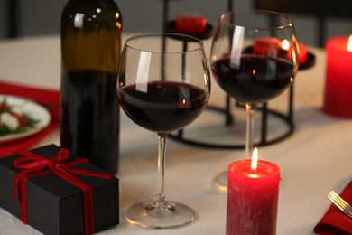 Photo of Red wine, burning candles and gift box on table, closeup. Romantic dinner