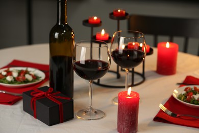 Photo of Red wine, burning candles and gift box on table, closeup. Romantic dinner