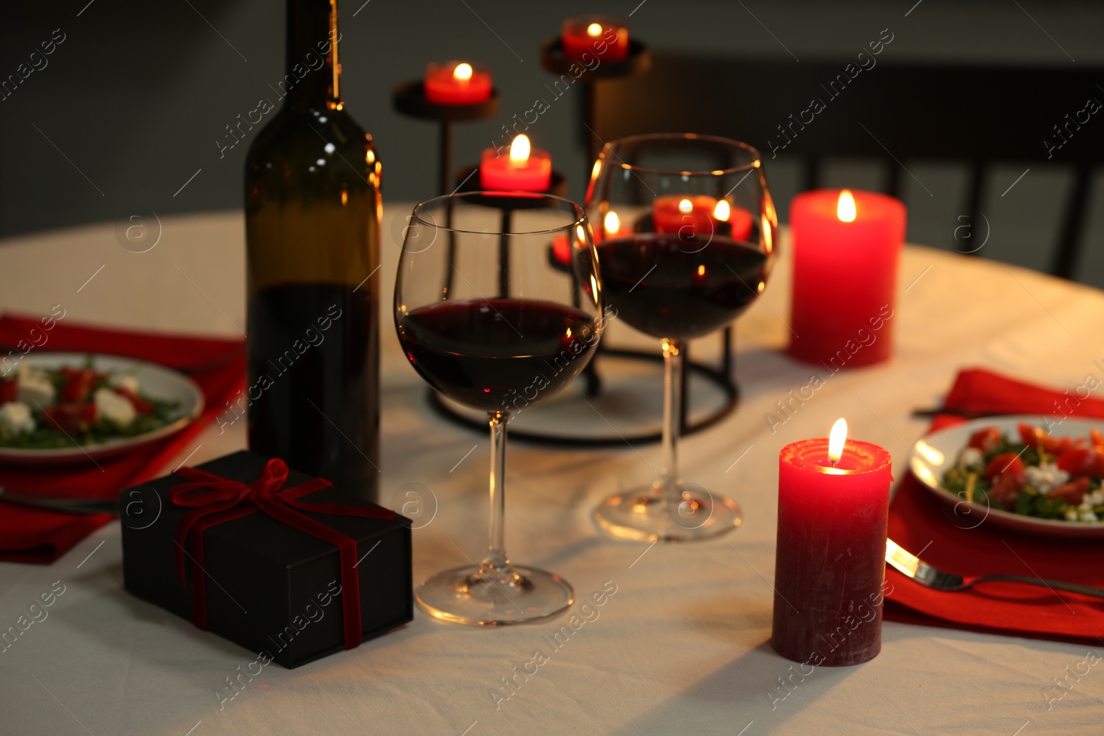 Photo of Red wine, burning candles and gift box on table. Romantic dinner