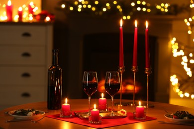 Photo of Romantic table setting with red wine and burning candles against blurred lights