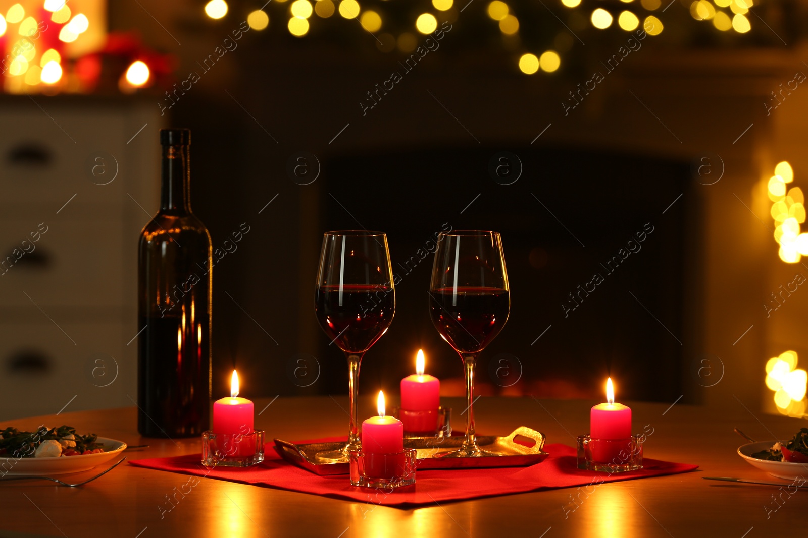 Photo of Romantic table setting with red wine and burning candles against blurred lights