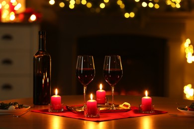 Photo of Romantic table setting with red wine and burning candles against blurred lights