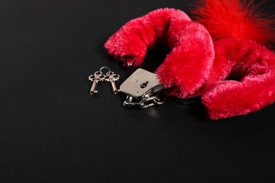 Photo of Bright fluffy handcuffs, keys and red feather on black background, space for text