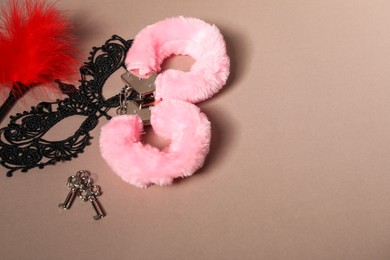 Photo of Pink fluffy handcuffs, lace mask, keys and feather on dark beige background