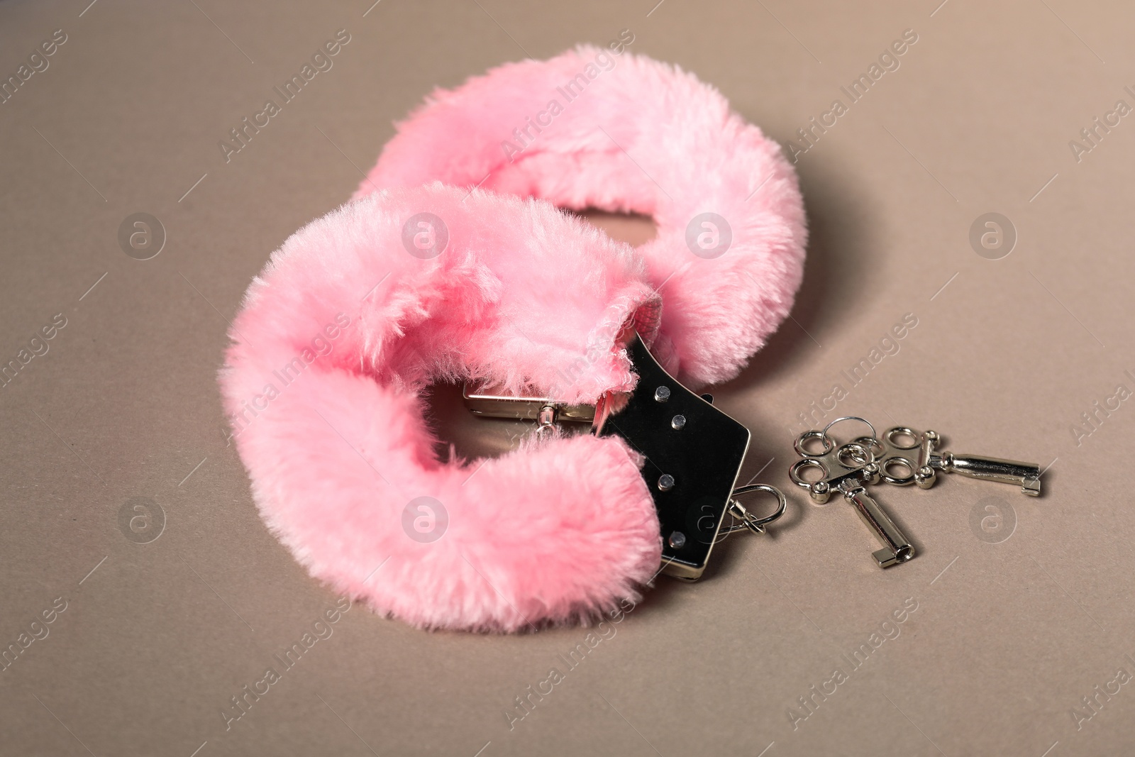 Photo of Pink fluffy handcuffs and keys on dark beige background