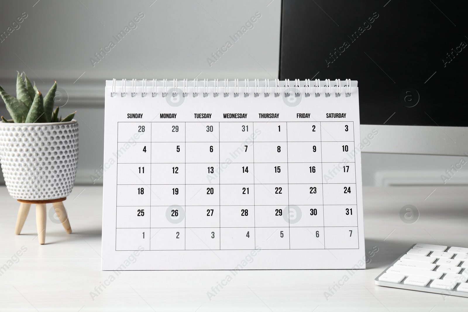 Photo of Timetable. Monthly planner, floral decor and computer on white table